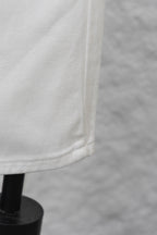 White denim pant leg with visible seam and bottom edge, close-up