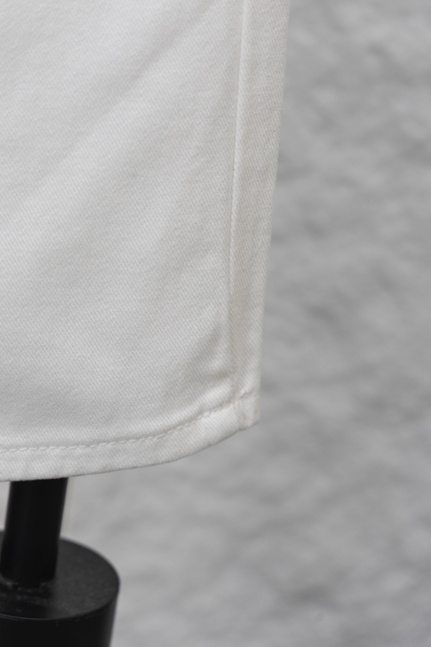 White denim pant leg with visible seam and bottom edge, close-up