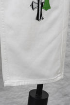 White denim skirt-like hem detail with green and black cactus-style patch, close-up
