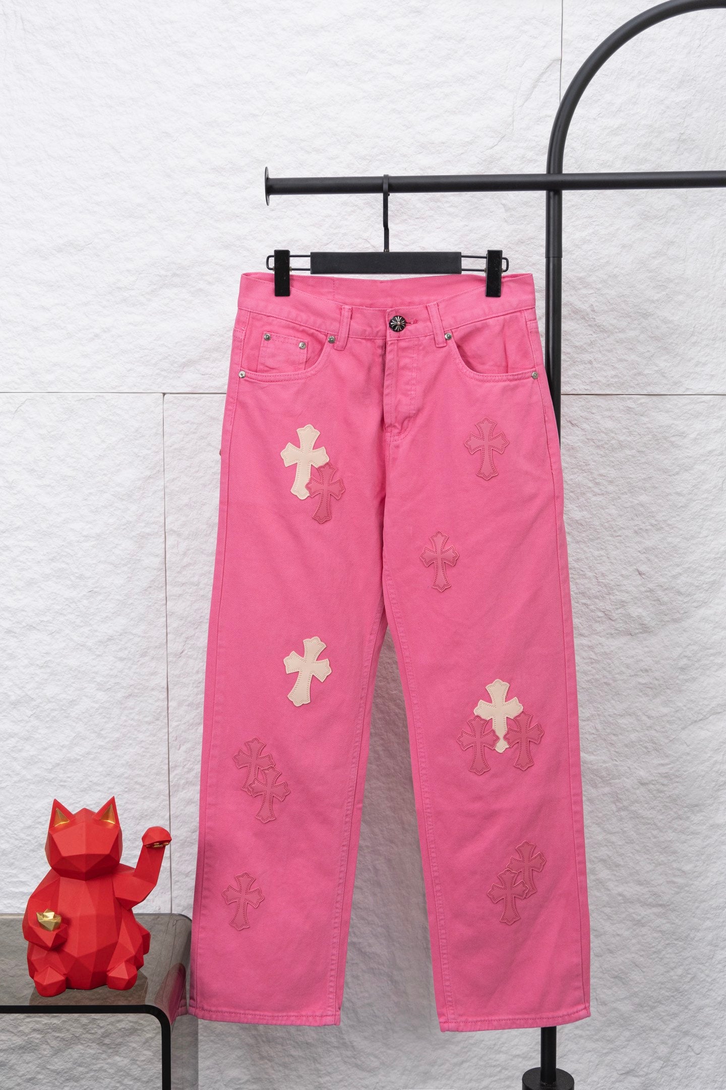 Pink denim pants with belt loops and button closure, featuring light cross patches
