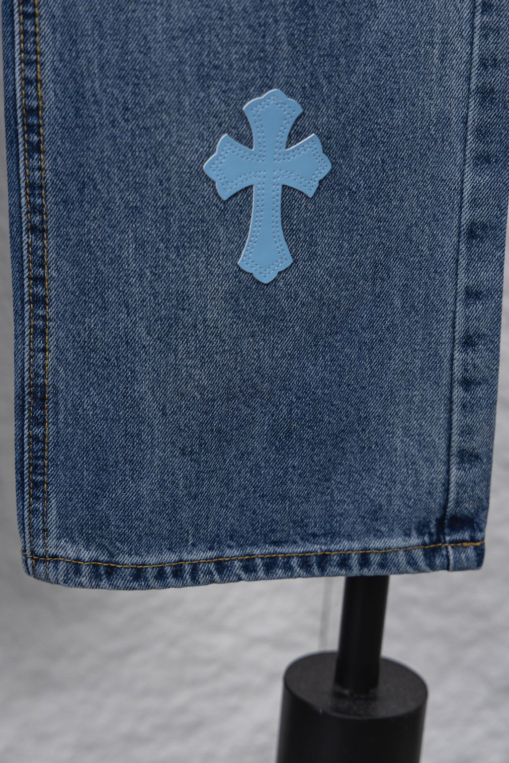 Light blue denim fabric with a blue cross patch near the hem