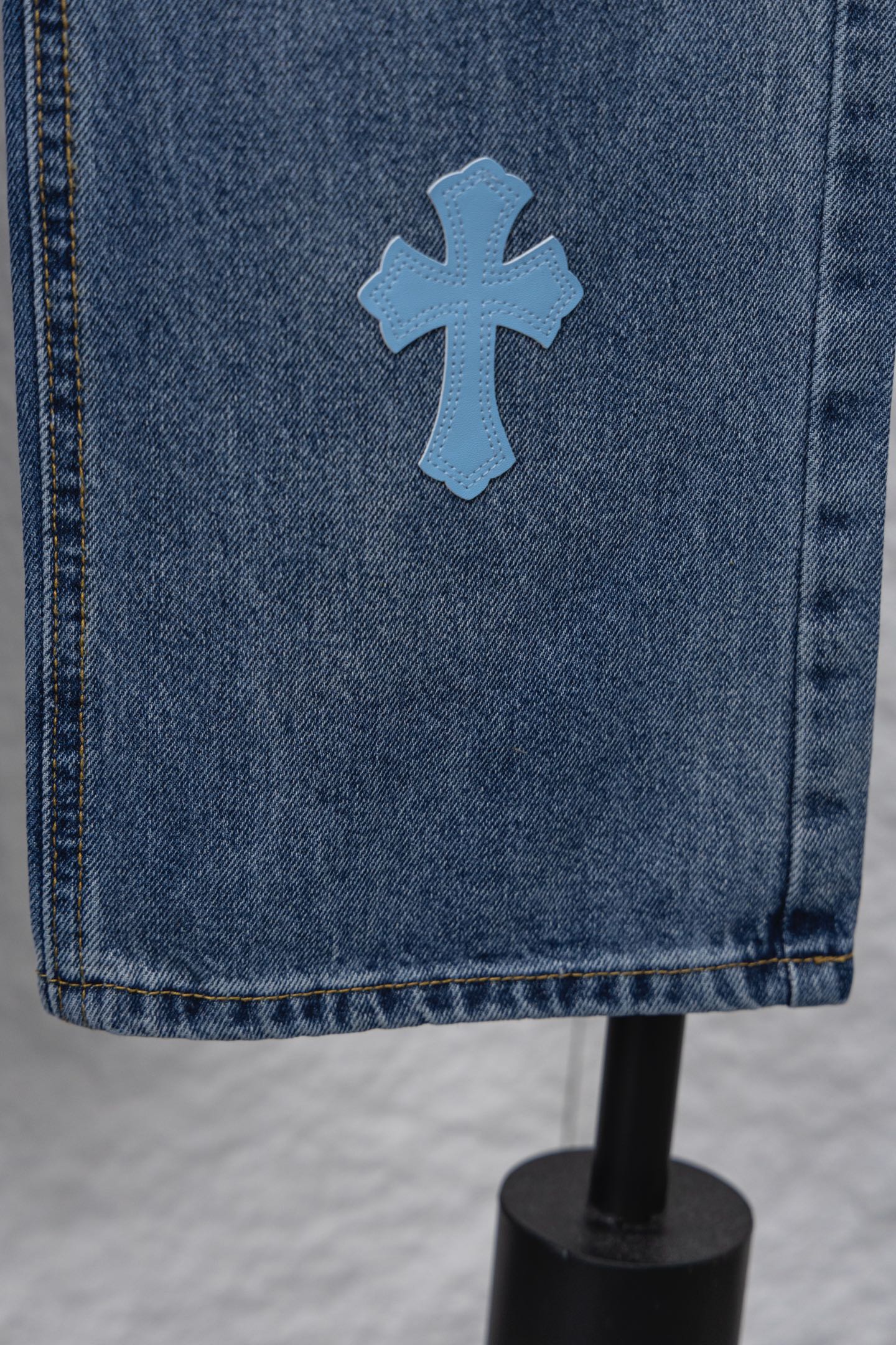 Light blue denim fabric with a blue cross patch near the hem