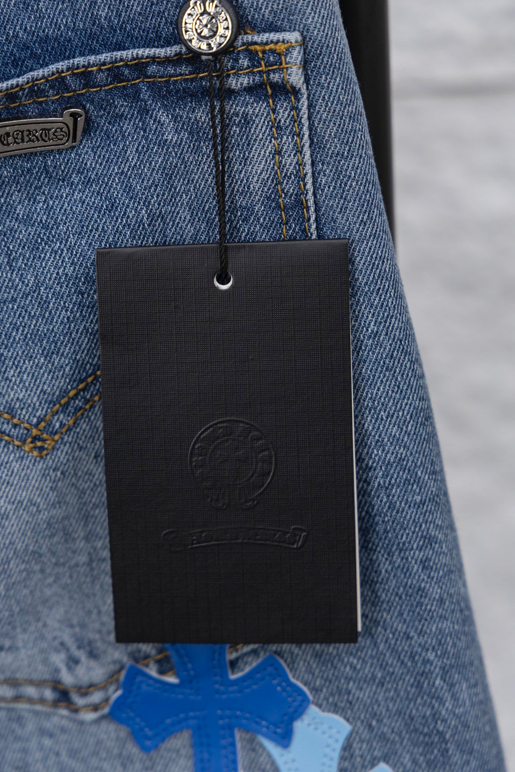 Light blue denim with a hanging black brand tag near the pocket