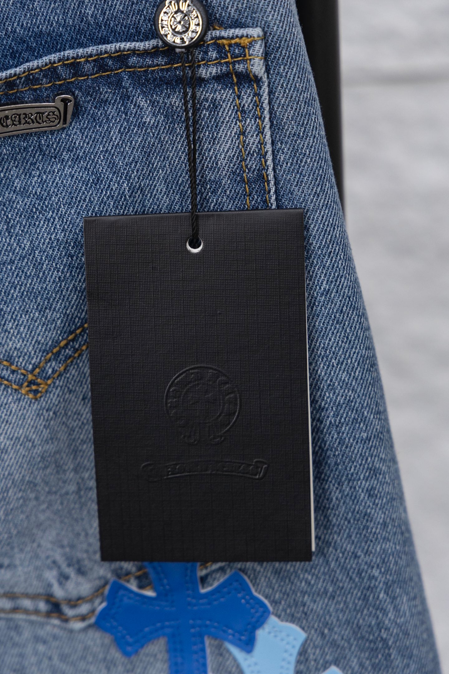 Light blue denim with a hanging black brand tag near the pocket