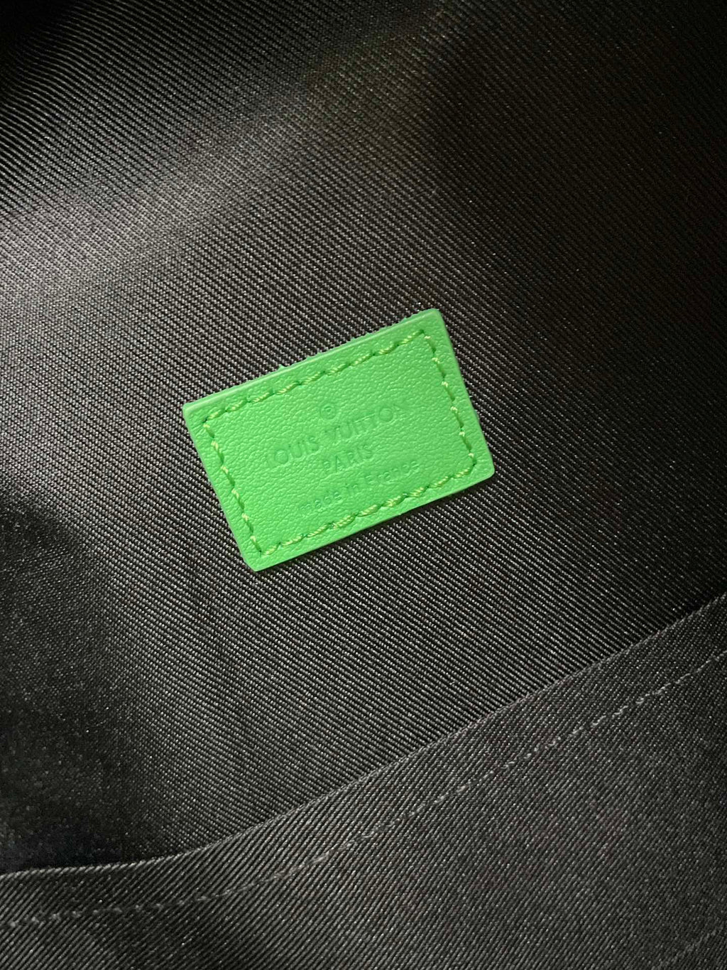 Louis Vuitton bag with neon-green label patch on dark fabric interior
