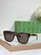 Gucci sunglasses with dark brown frame and tinted lenses, gold-toned temple accents.