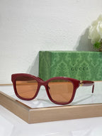 Gucci sunglasses with red frame and tinted lenses, gold-toned temple accents.
