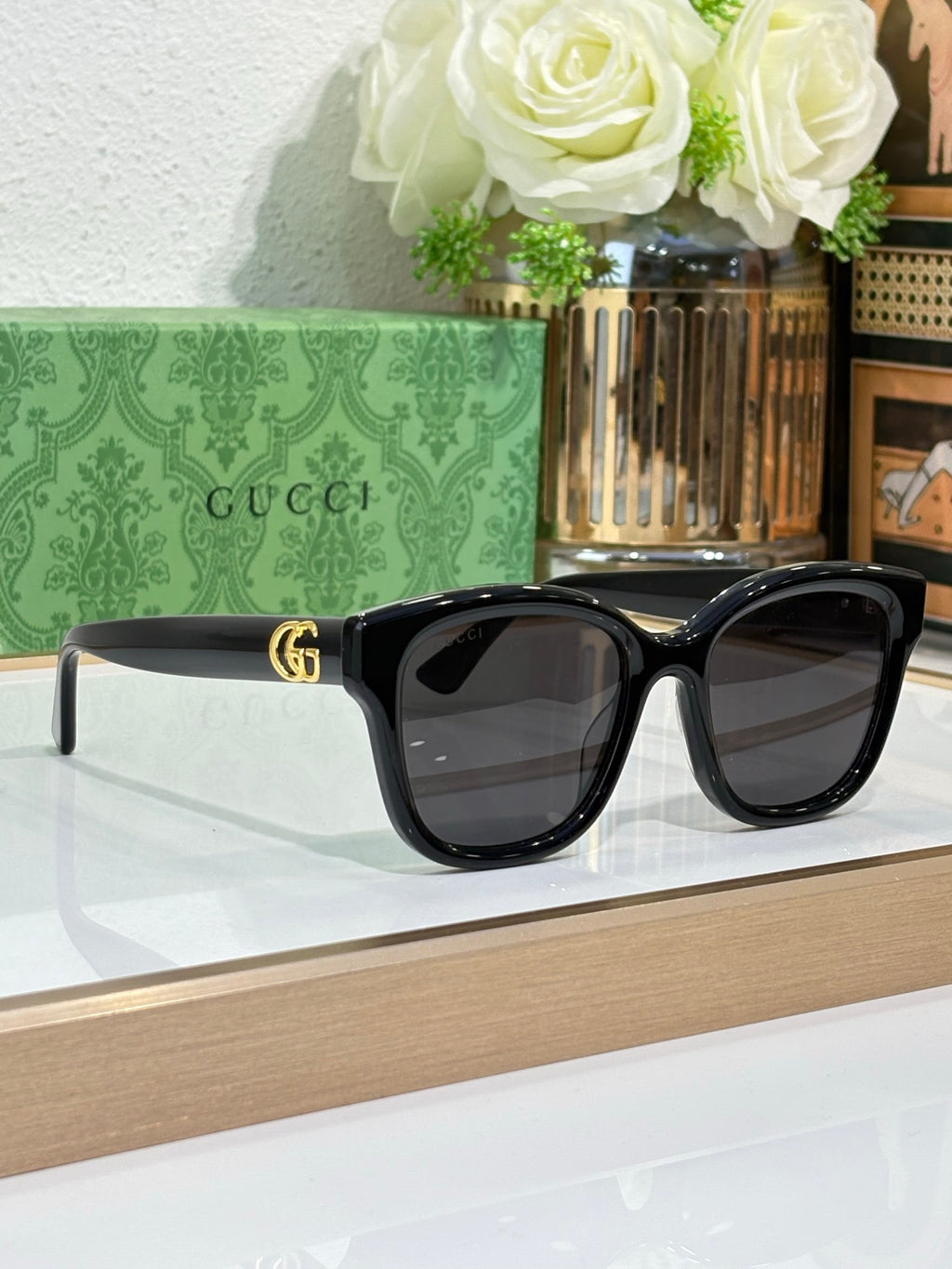 Gucci sunglasses with black frame and dark lenses, gold-toned GG-style logo.