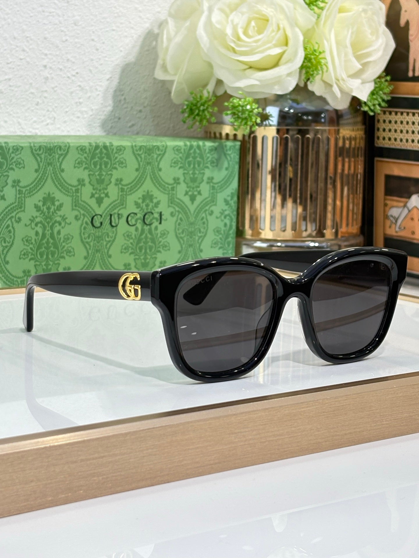 Gucci sunglasses with black frame and dark lenses, gold-toned GG-style logo.