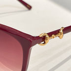 Gucci sunglasses close-up: maroon frame with gold hinge detail and rose tinted lens