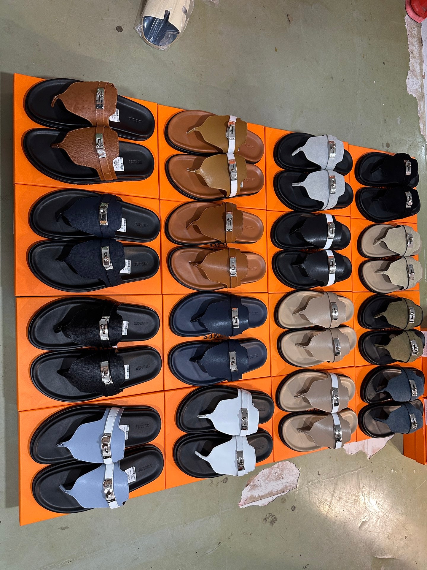 Assorted buckle slide sandals on orange box lids, in multiple colors and styles