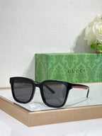Sunglasses by Gucci with black oversized frames and dark tinted lenses on a display tray.