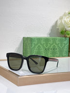 Sunglasses by Gucci with black oversized frames and dark tinted lenses on a display tray.