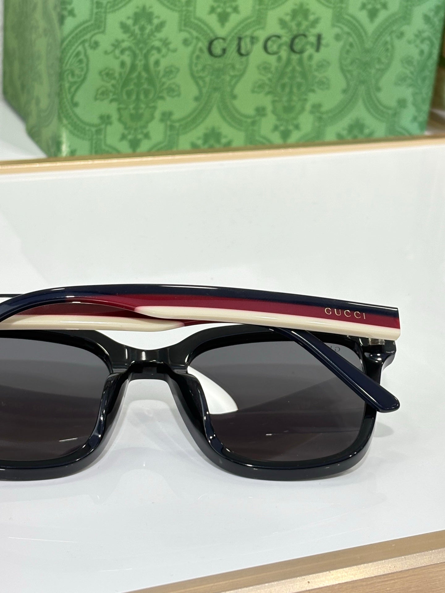 Sunglasses by Gucci with black frames and a red-accent top temple bar, side view.
