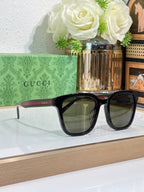 Sunglasses by Gucci with black oversized frames and dark lenses; red and green temple tips.