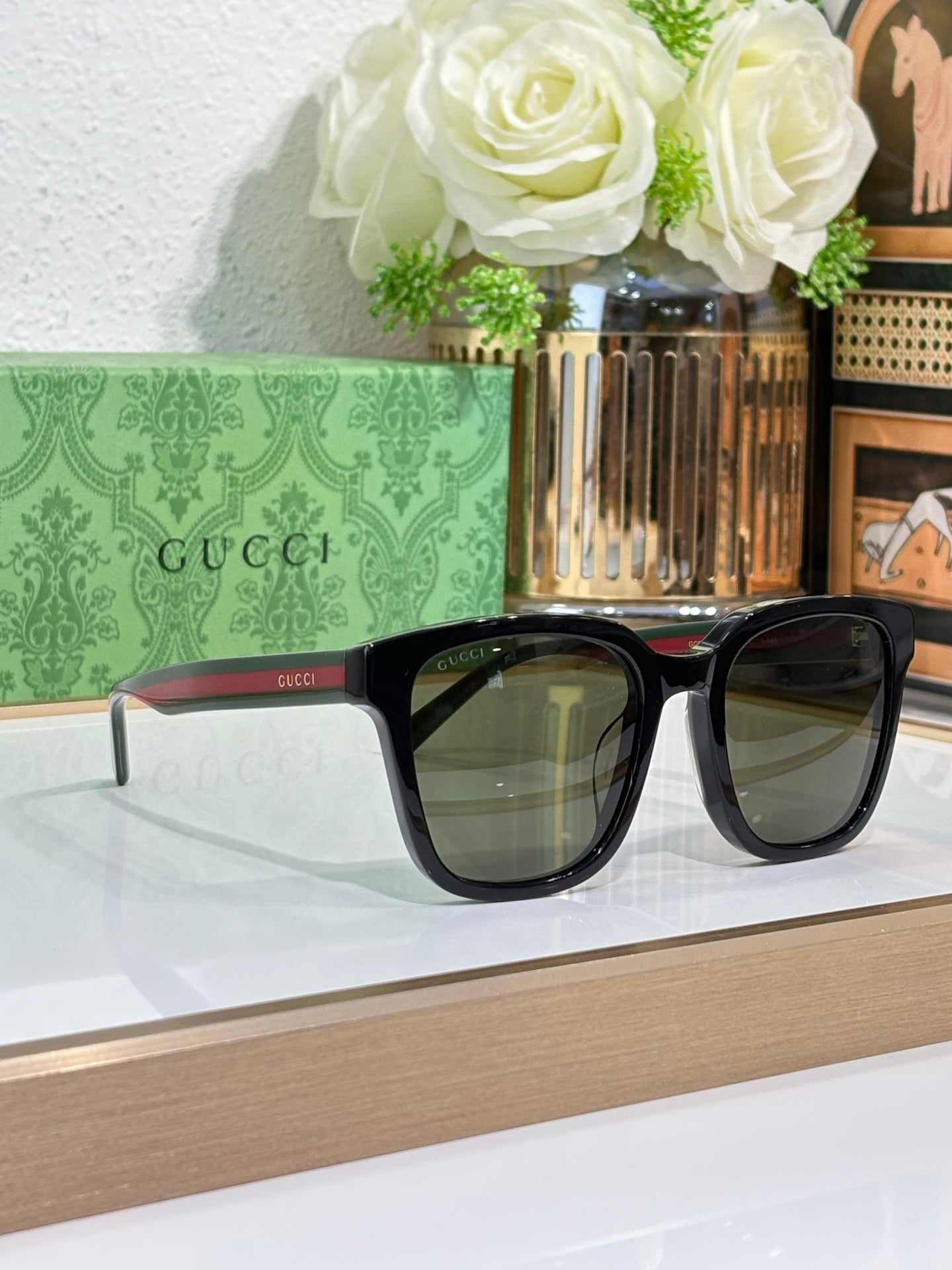 Sunglasses by Gucci with black oversized frames and dark lenses; red and green temple tips.