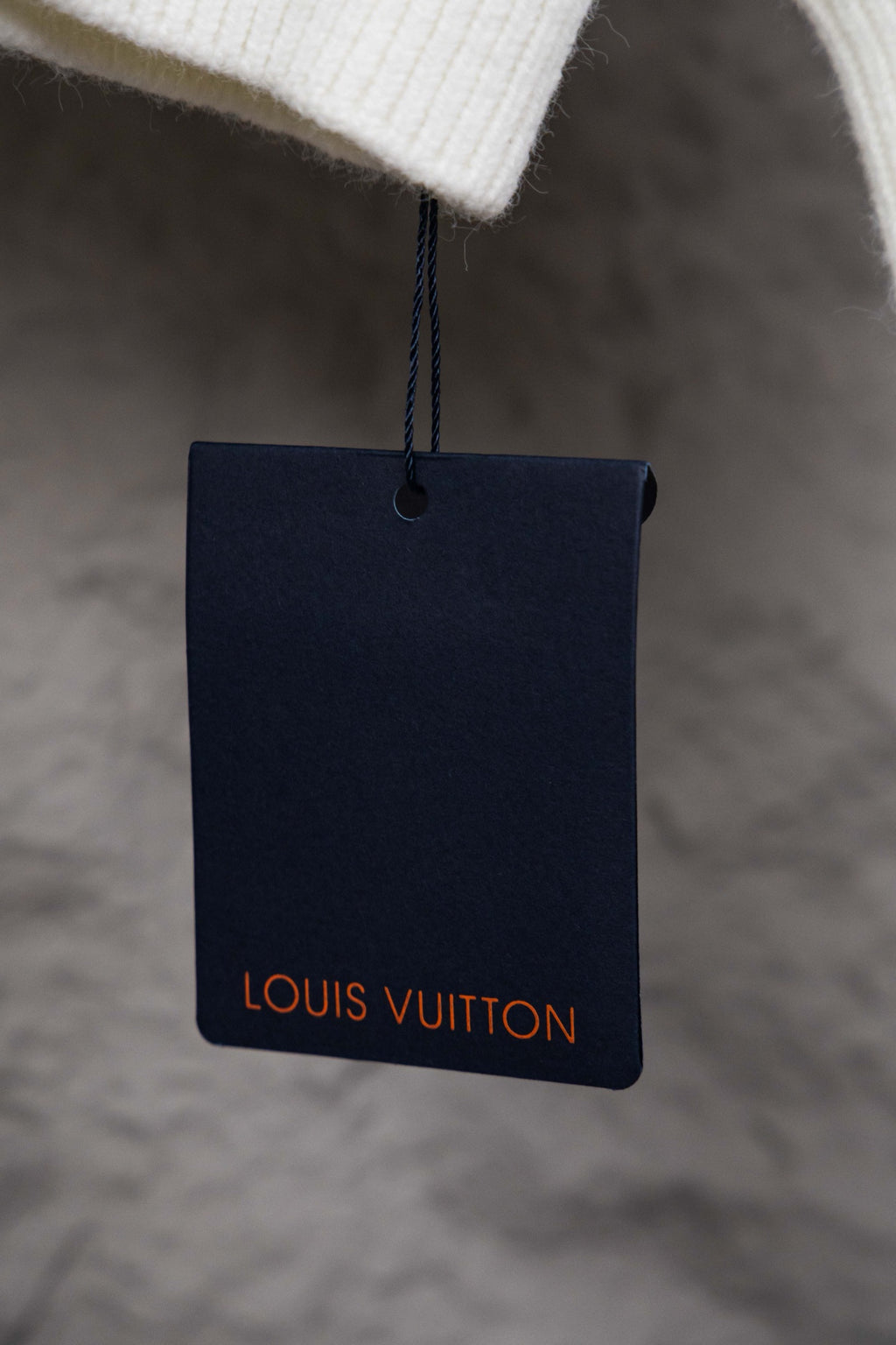 Navy hang tag on white sweater, Louis Vuitton logo in red text
