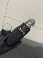 Gucci black horsebit mule held at angle, gold hardware and embossed logo-style trim