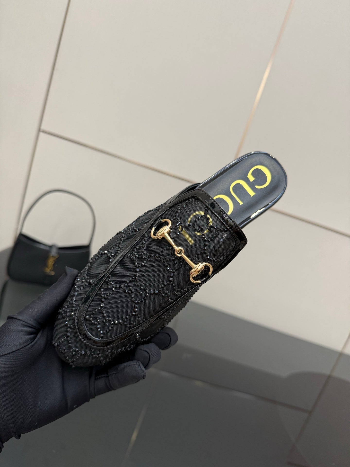 Gucci black horsebit mule held at angle, gold hardware and embossed logo-style trim