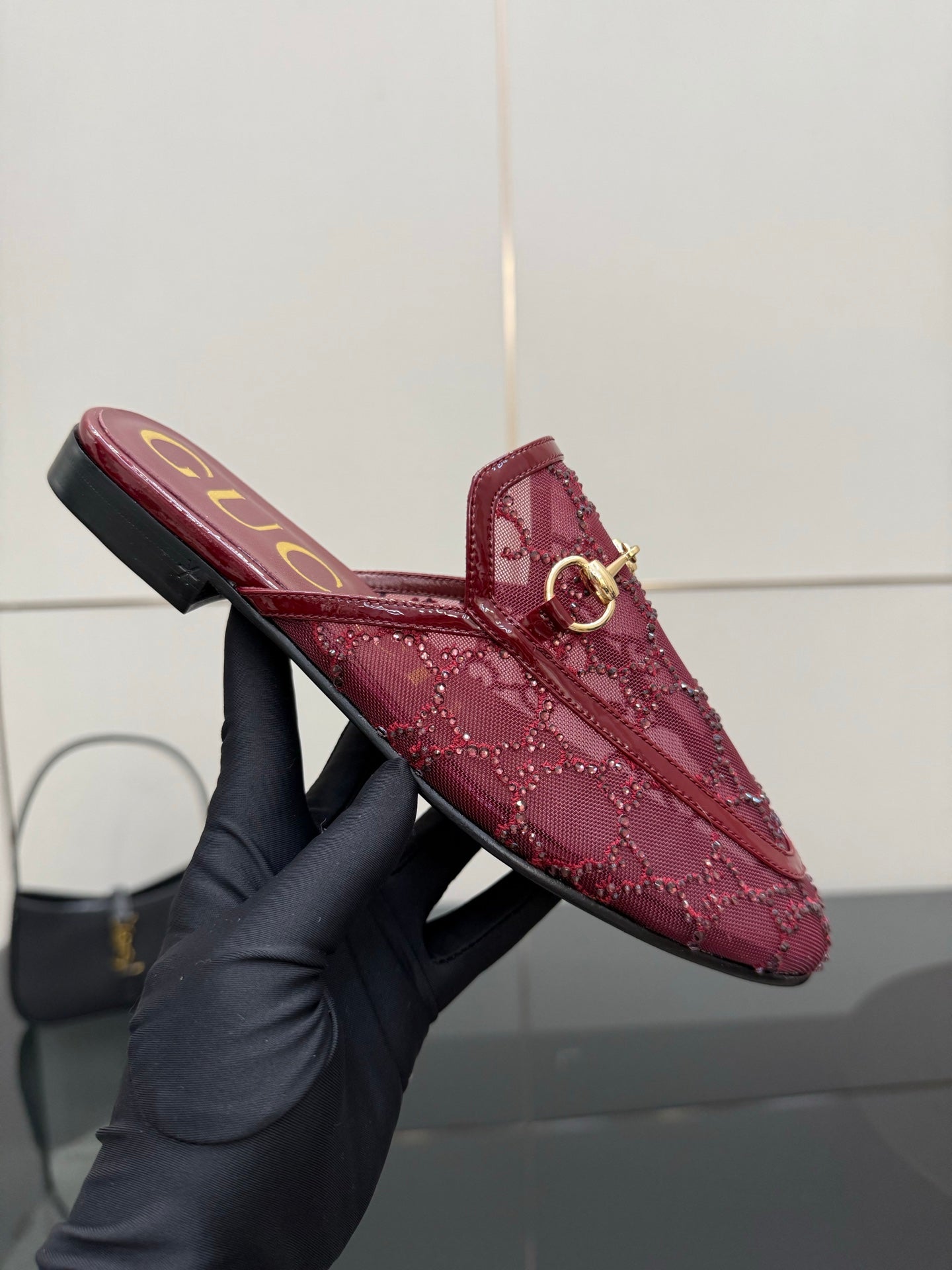 Gucci women's burgundy loafers with gold horsebit, held by a gloved hand