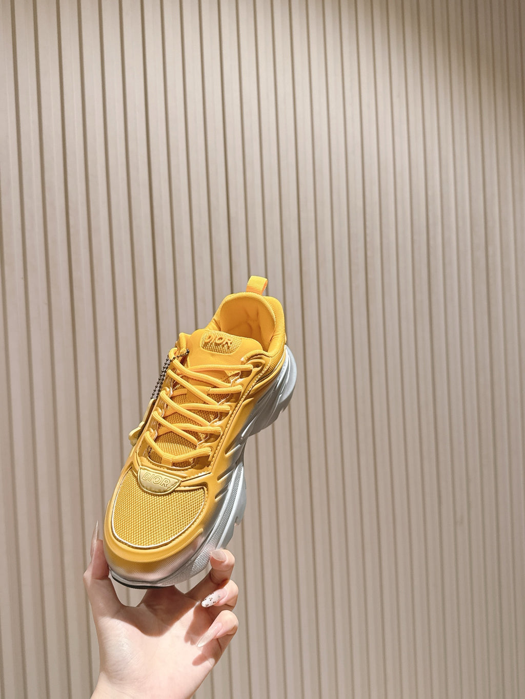 Dior unisex sneaker held up, yellow lace-up upper with silver midsole detail