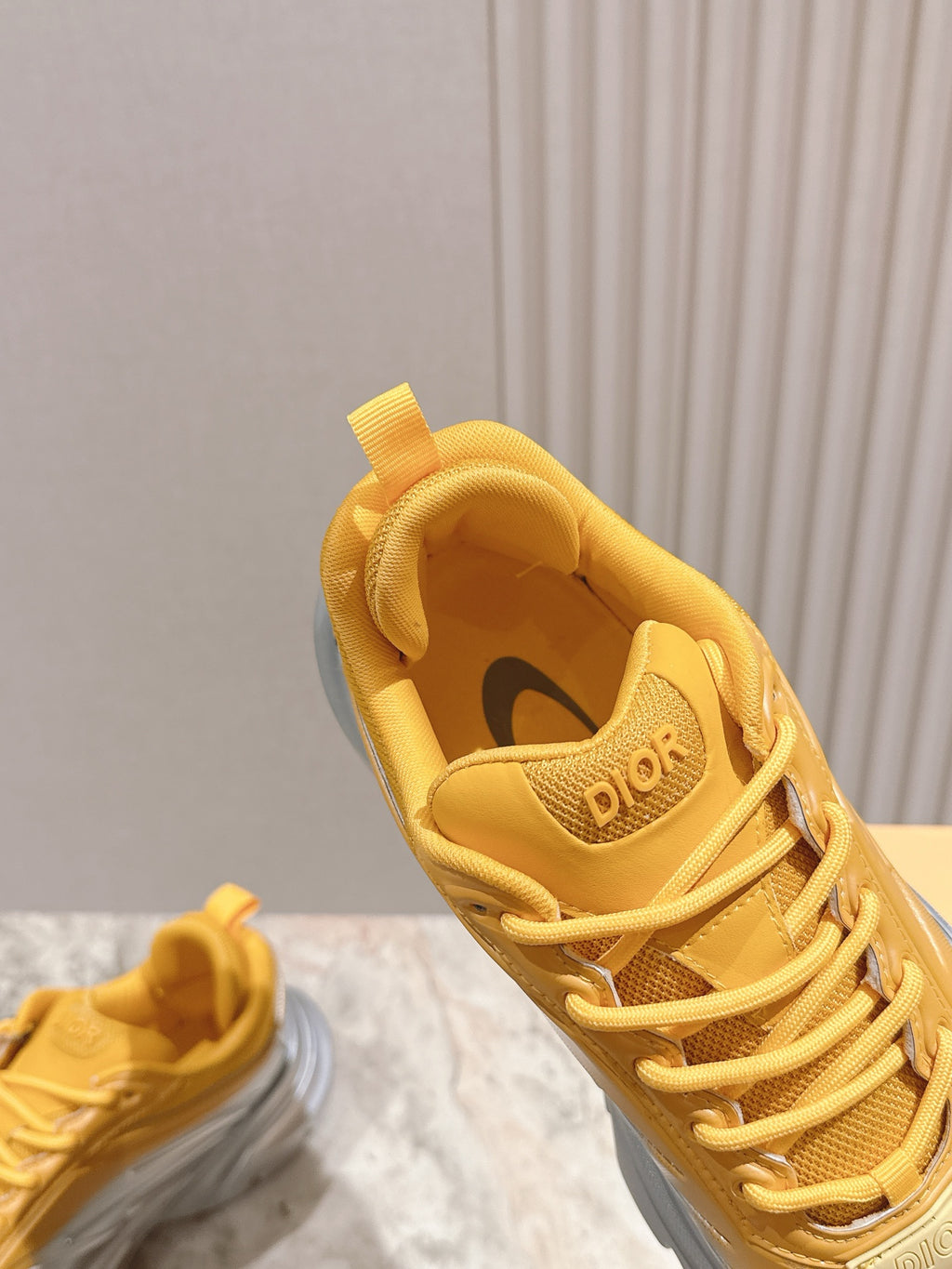 Dior unisex sneaker upper close-up, yellow lace and tongue with “Dior” logo