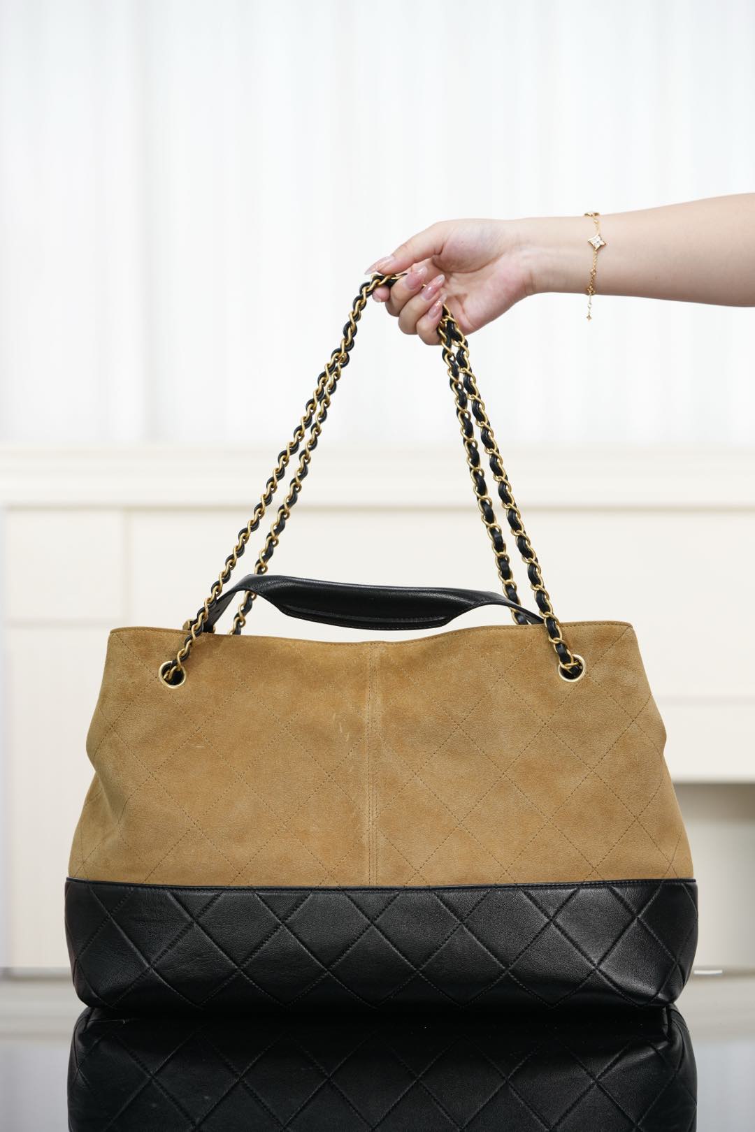 Two-tone Chanel shoulder tote with tan front and quilted black base, held by chain handles.