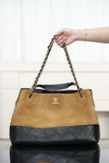 Two-tone Chanel shoulder tote with tan body, quilted black base, gold-tone chain handles.