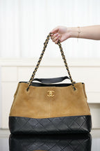 Two-tone Chanel shoulder tote with tan body, quilted black base, gold-tone chain handles.