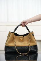 Two-tone Chanel tote bag held by top handles; tan body with quilted black base.