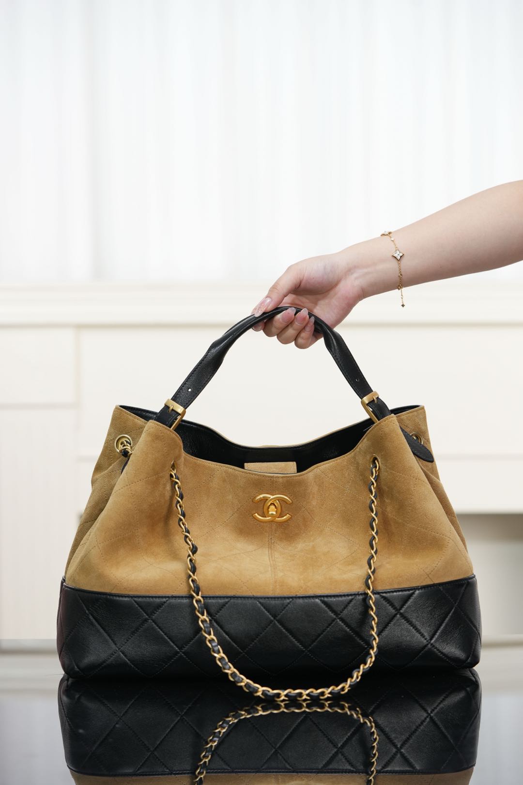 Two-tone Chanel tote bag held by top handles; tan body with quilted black base.