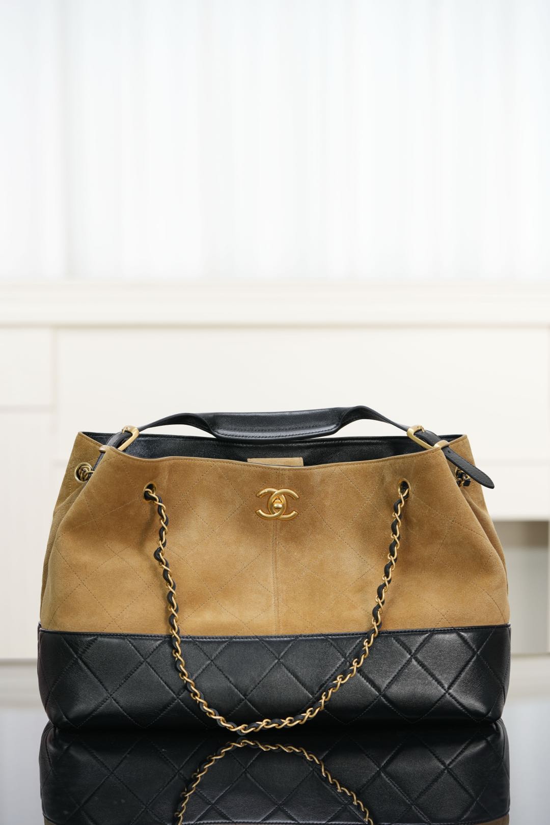 Two-tone tote bag: tan suede-style top, quilted black base, chain straps, Chanel logo.