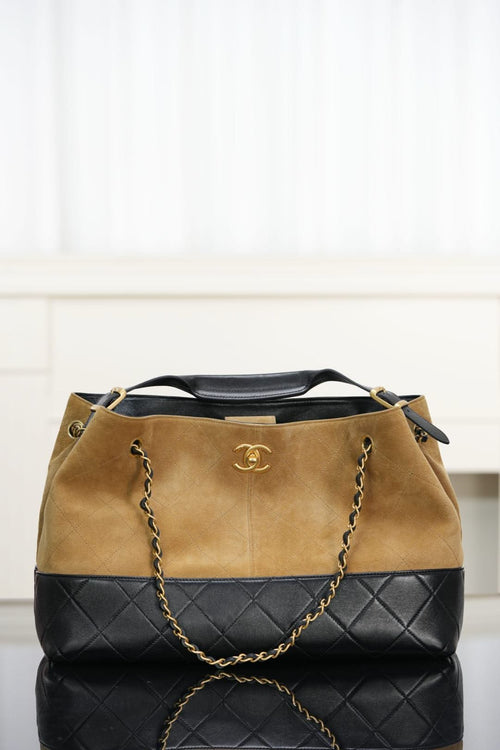Two-tone tote bag: tan suede-style top, quilted black base, chain straps, Chanel logo.
