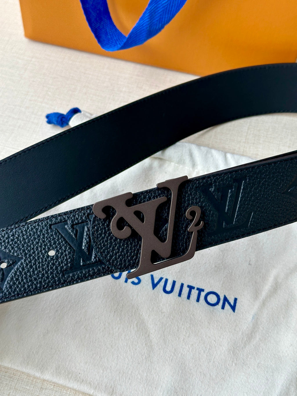 Black leather belt close-up showing embossed pattern and metal LV buckle