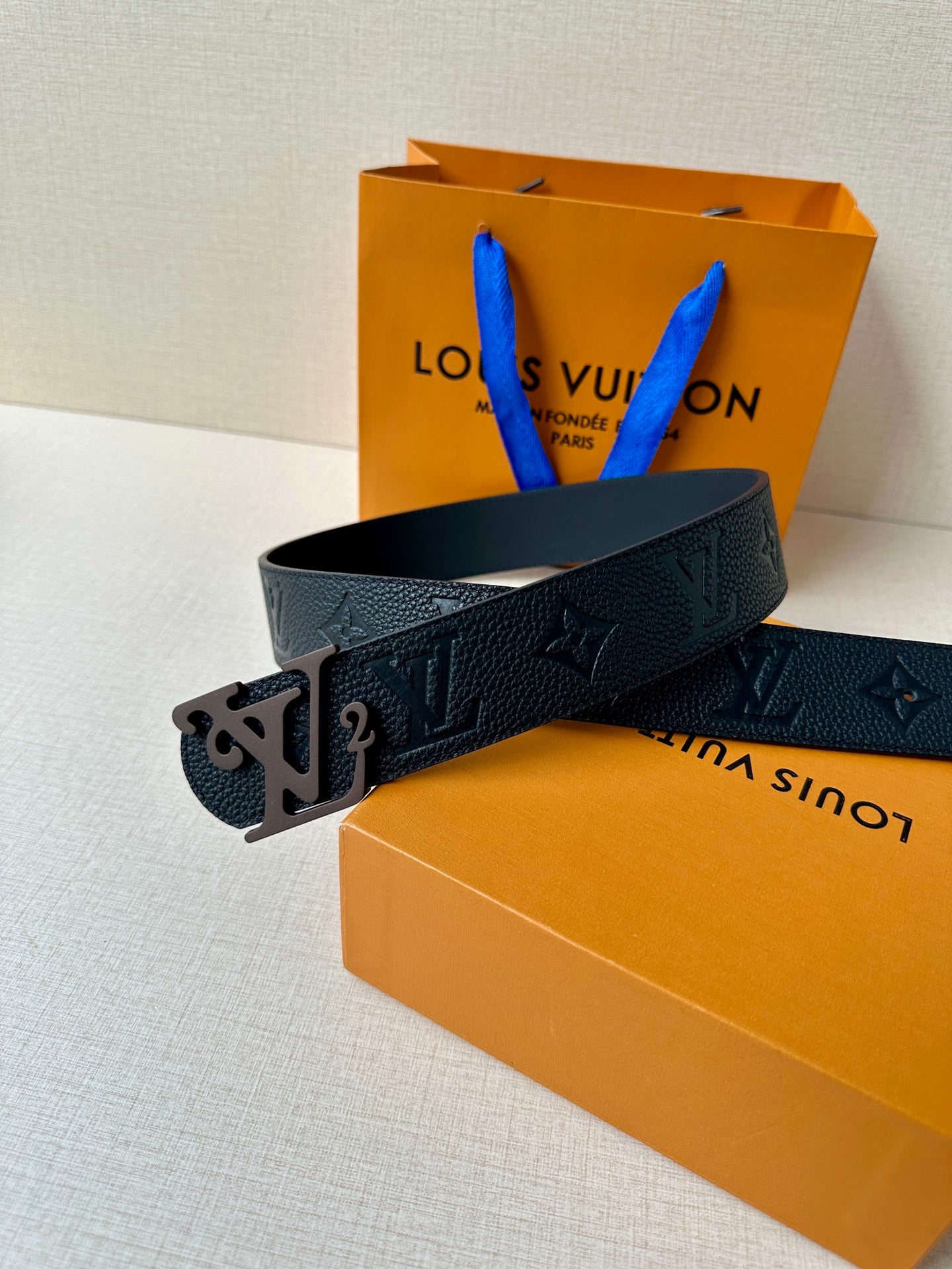 Black textured leather belt with embossed monogram and metal LV buckle, side view