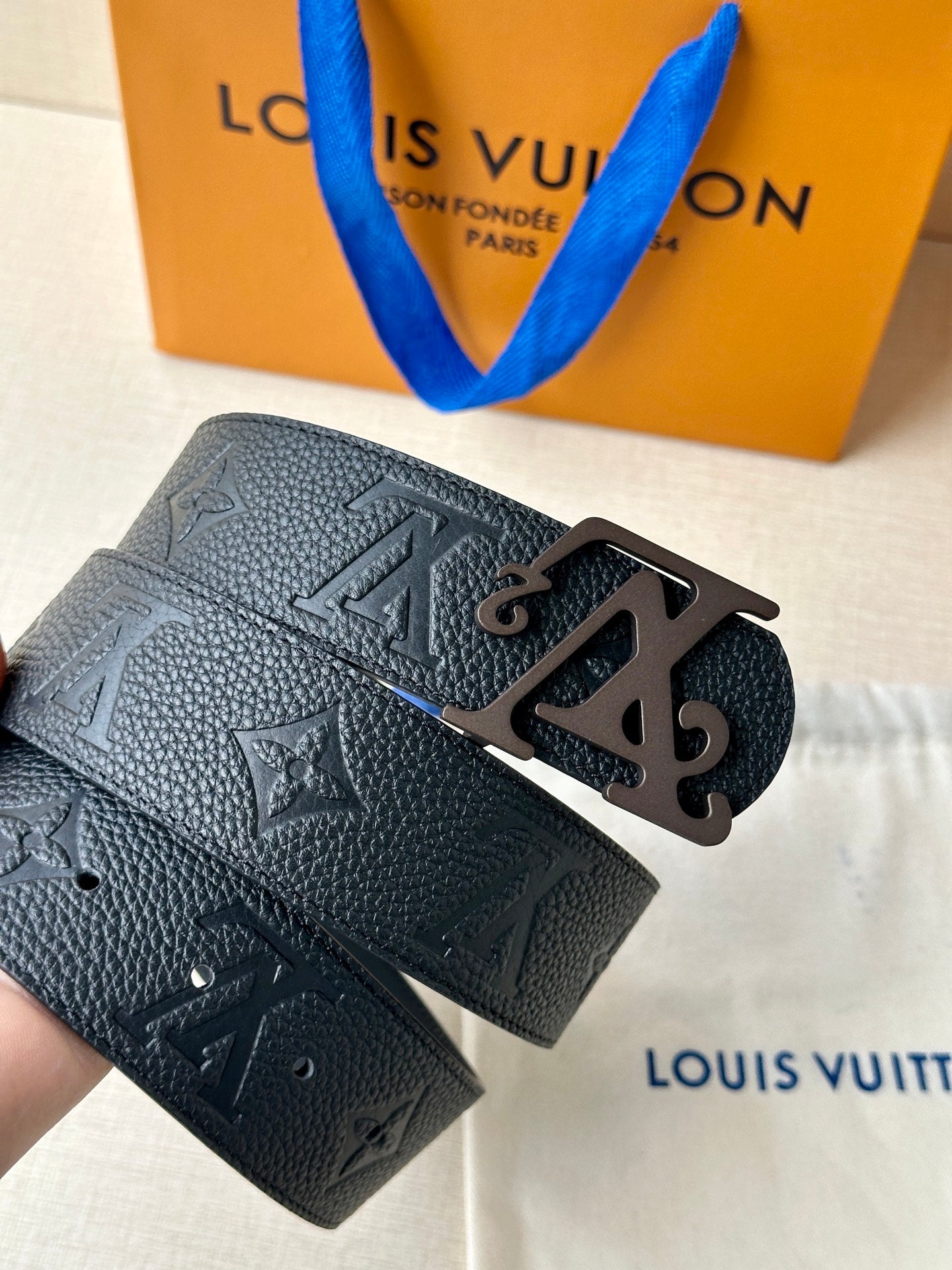 Black leather belt with embossed monogram and metal LV buckle, angled view