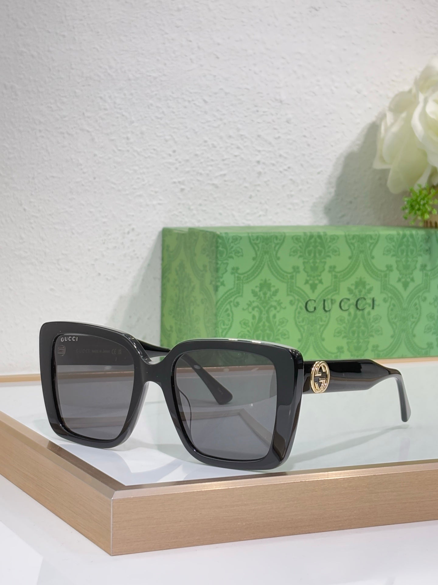 Black square sunglasses with gray lenses on display with temple logo detail.