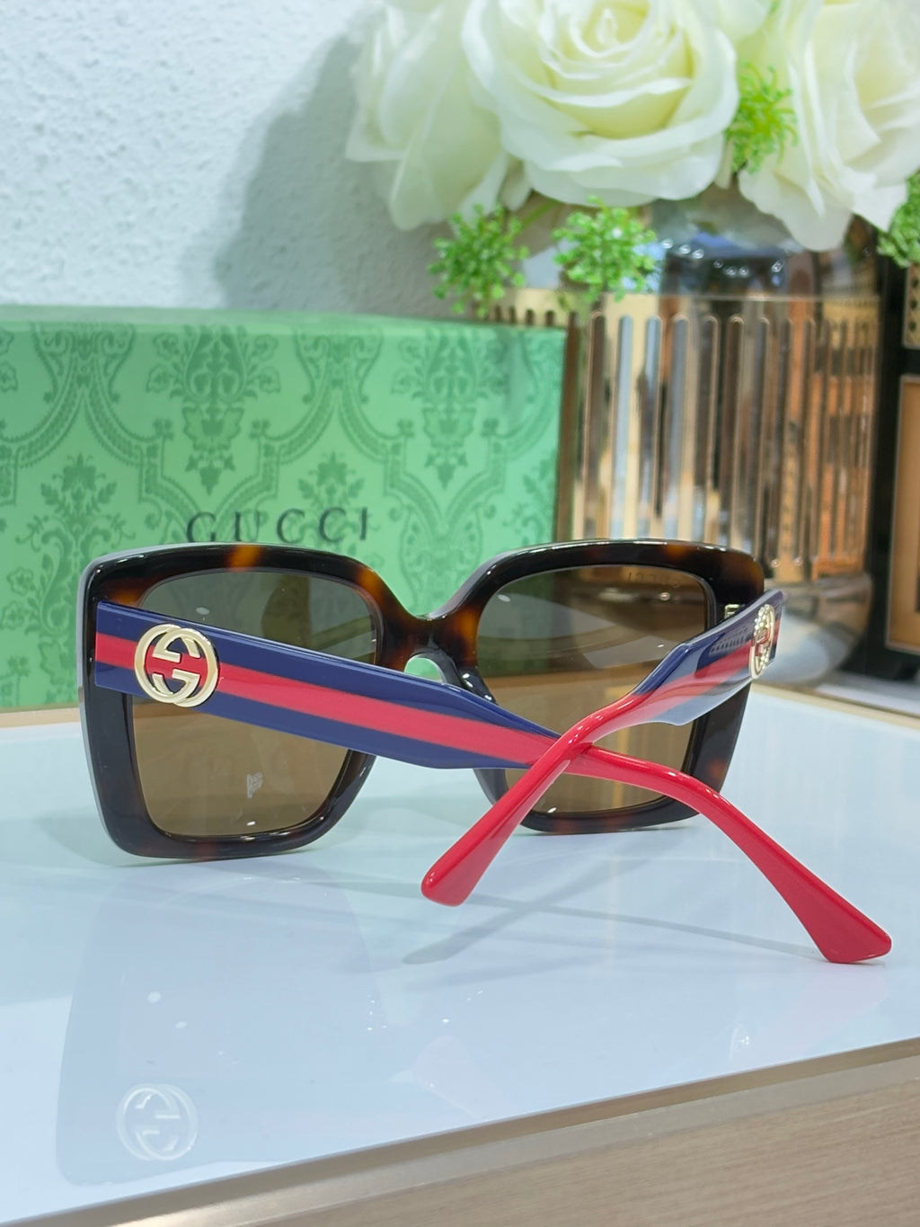 Square sunglasses with tortoise frame, blue/red striped temples, and gold logo detail.