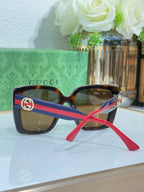 Square sunglasses with tortoise frame, blue/red striped temples, and gold logo detail.