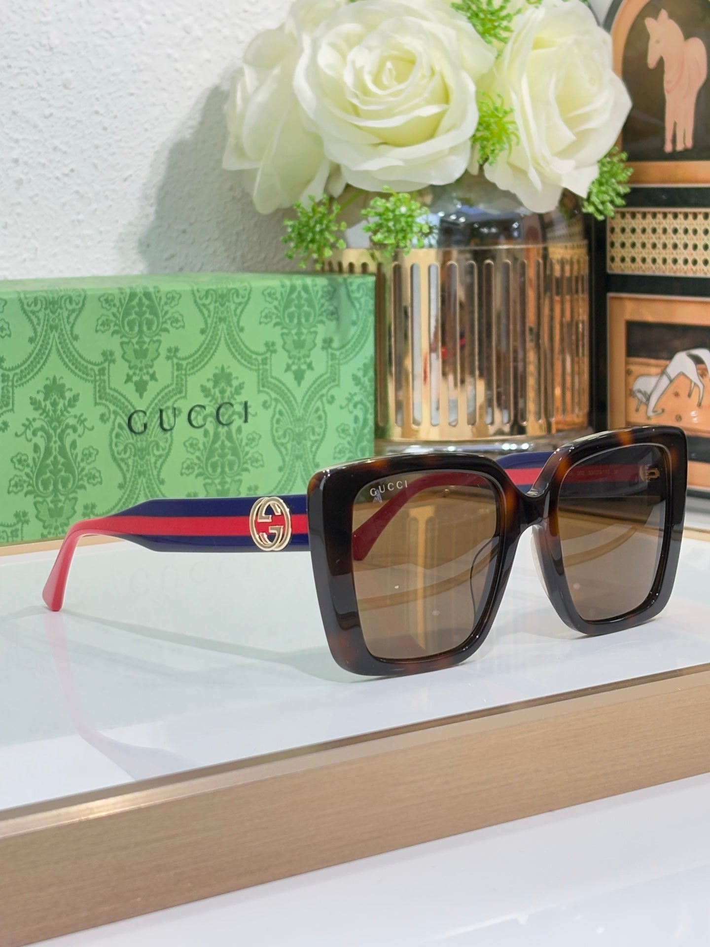 Square sunglasses with dark tortoise frame, gold logo hardware, and red temples.
