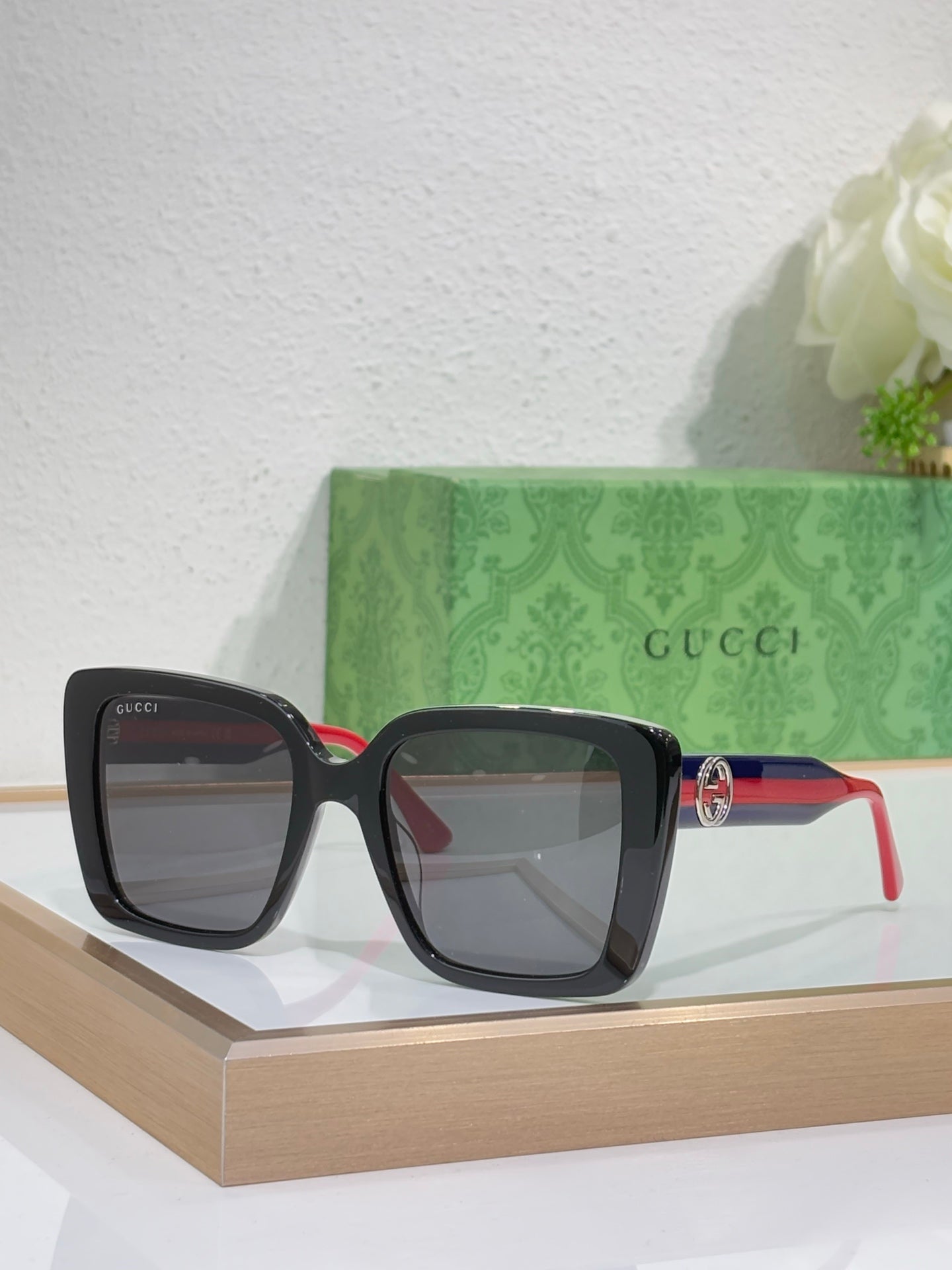 Black square sunglasses with gray lenses and red/green temple stripe.