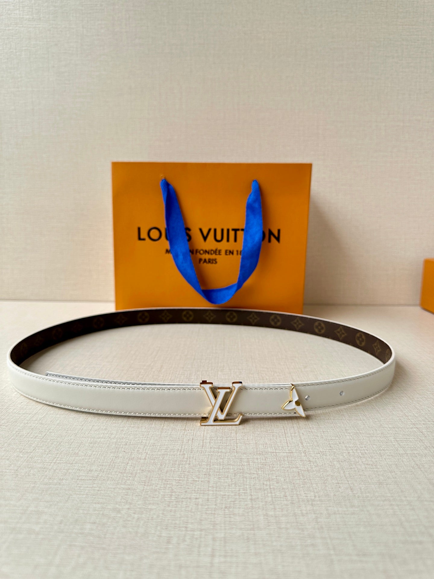 White leather belt with gold-tone LV buckle, lying flat.