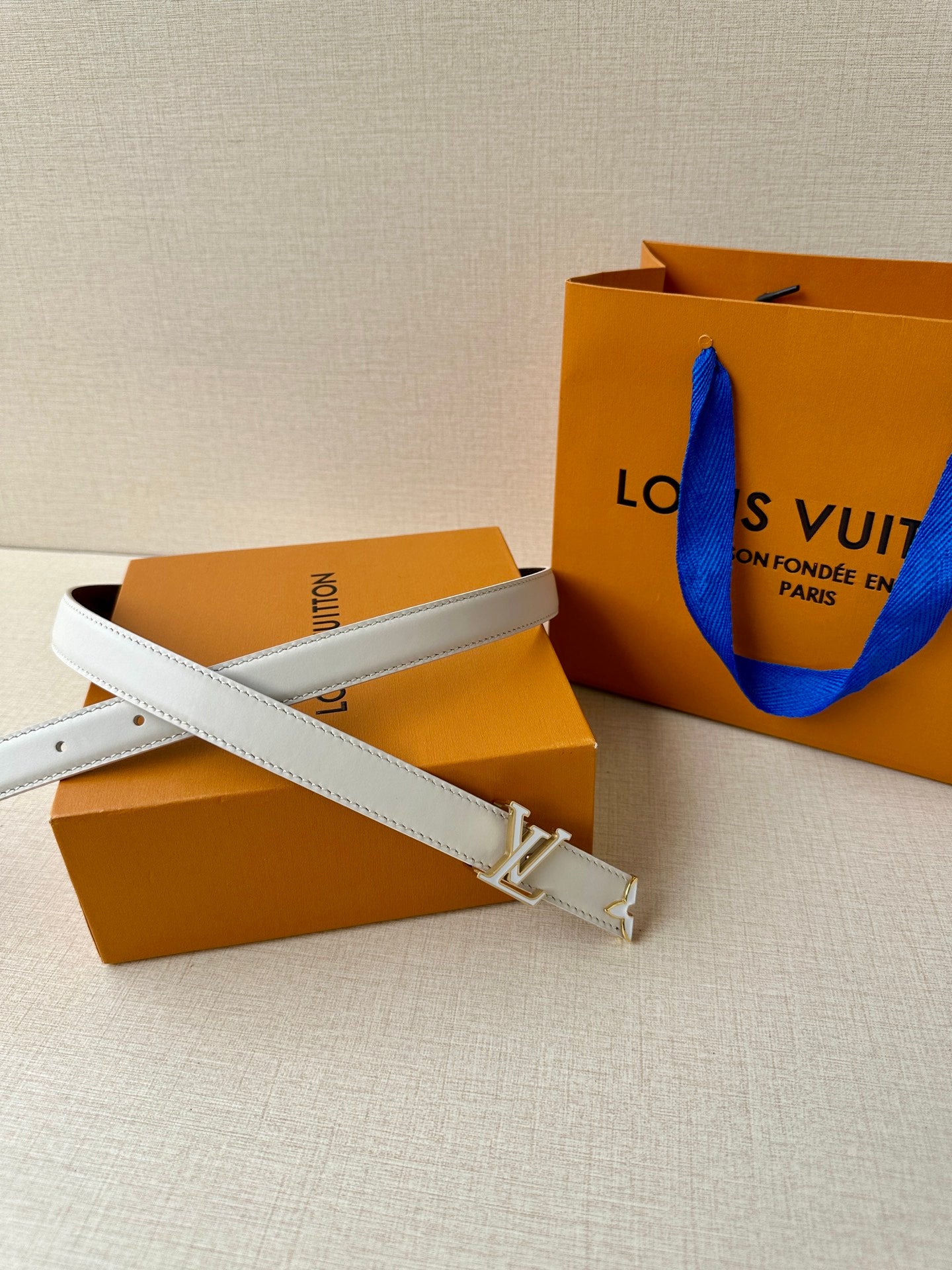 White leather belt with gold-tone LV buckle, belt end and keeper visible.