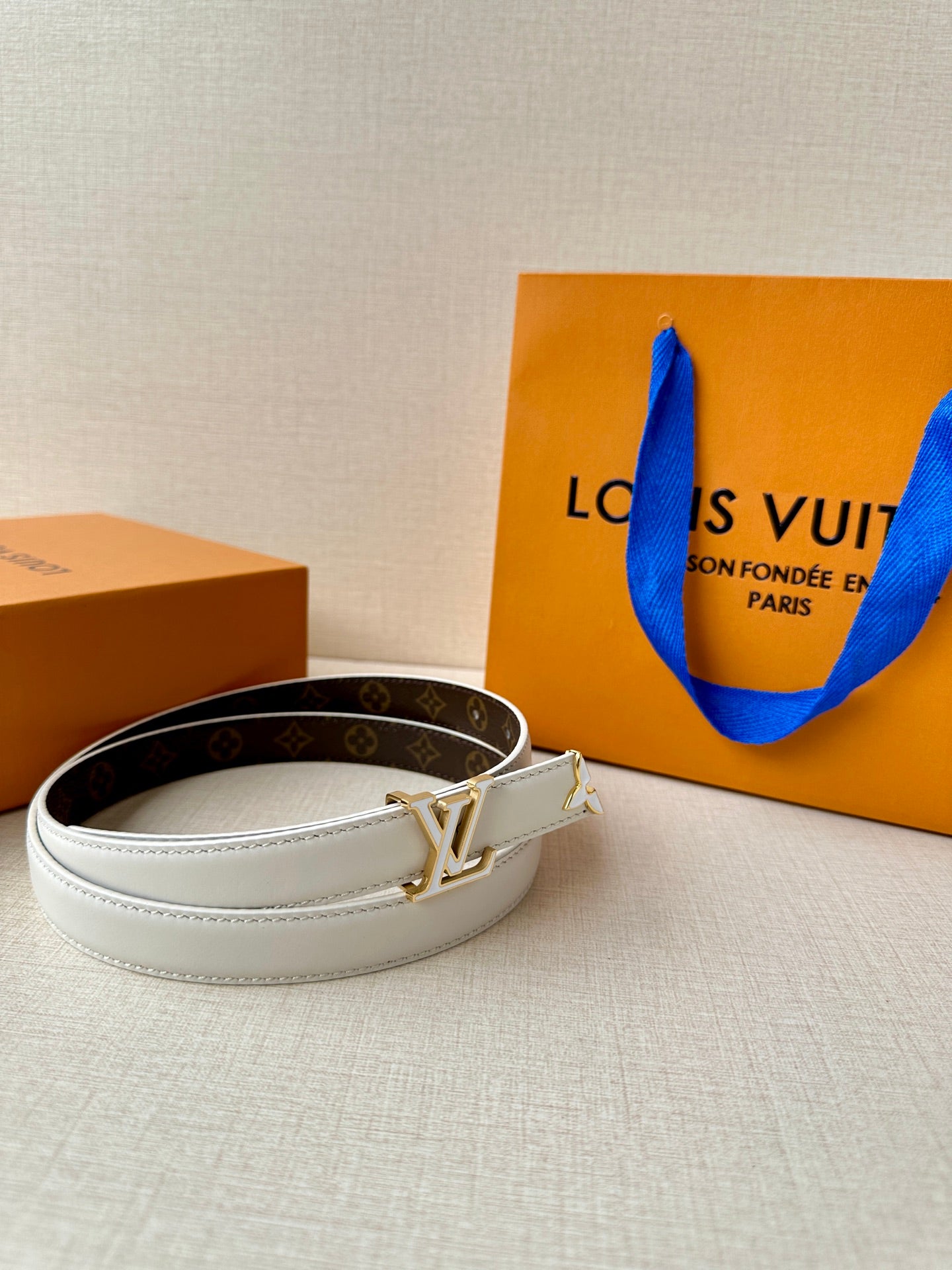White leather belt with gold-tone LV buckle, angled view with edge stitching.