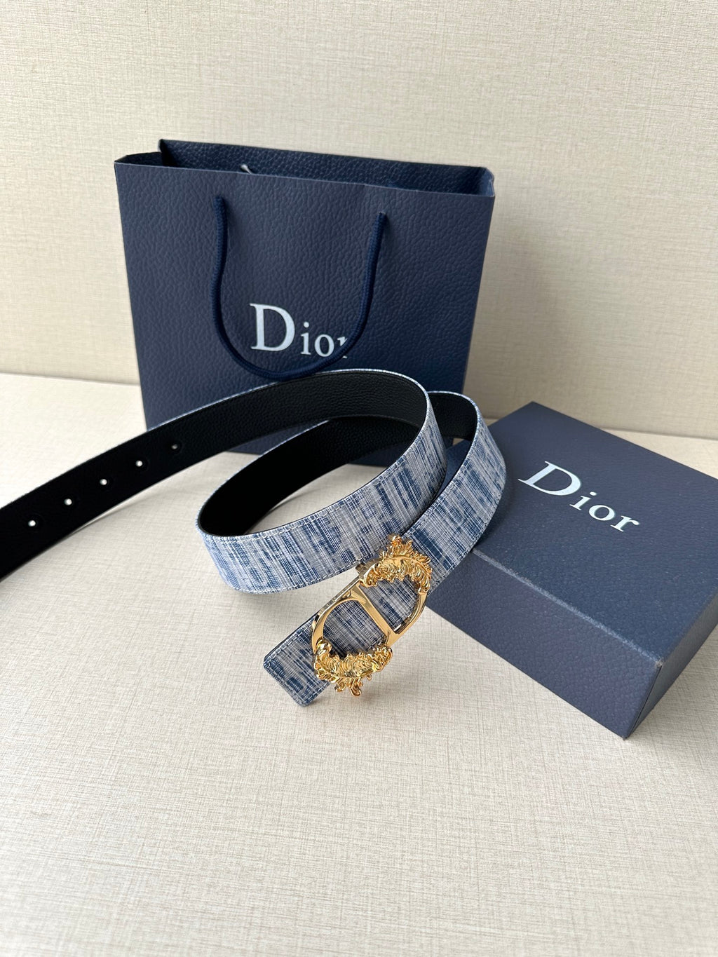 Dior belt with blue textured fabric strap and gold clasp buckle, shown on stand