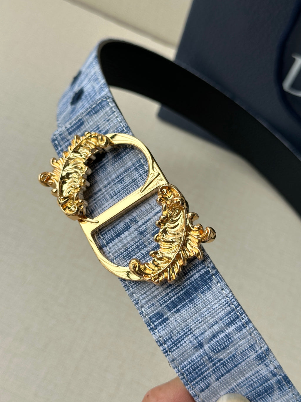 Dior belt buckle close-up on blue fabric weave strap with ornate gold frame