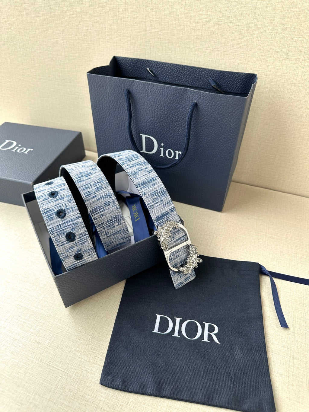 Dior belt in box with blue patterned strap and ornate gold buckle on navy pouch