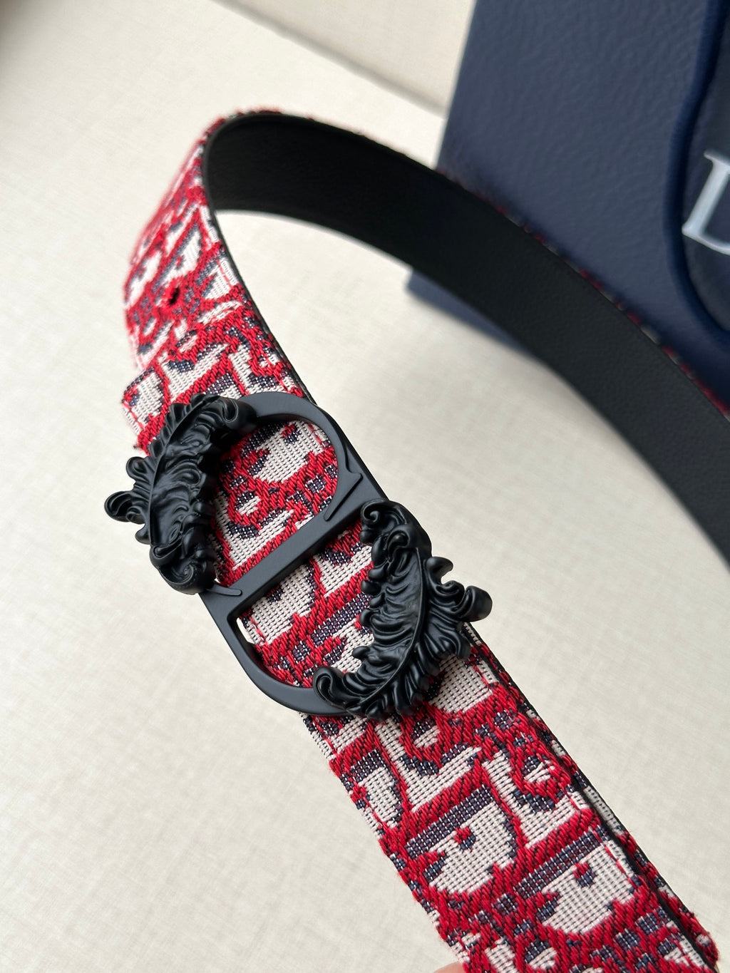 Dior belt close-up: red monogram strap with black buckle and floral appliqué.