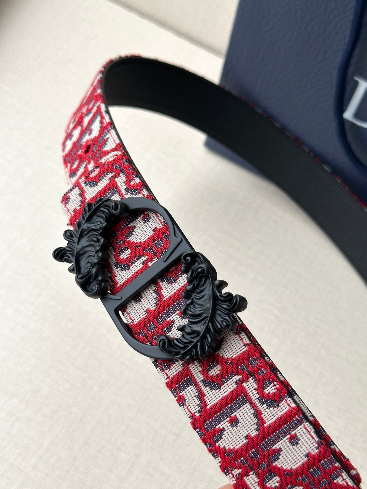 Dior belt close-up: red monogram strap with black buckle and floral appliqué.