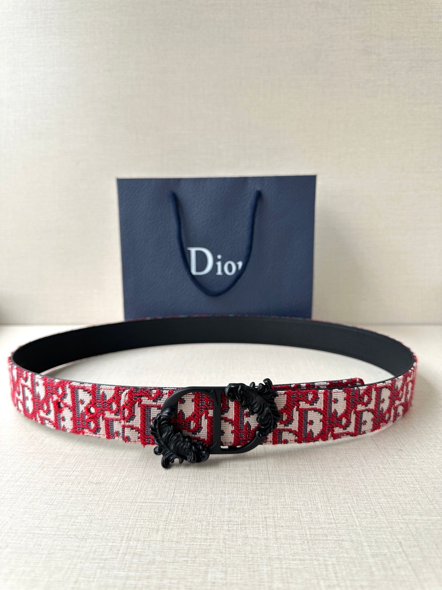 Dior belt with red-and-black monogram pattern and black buckle with floral detail.